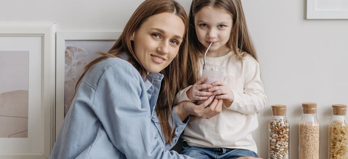 A loving mother with her daughter drinking a smoothie and sharing a warm moment in the kitchen.