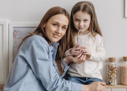 A loving mother with her daughter drinking a smoothie and sharing a warm moment in the kitchen.