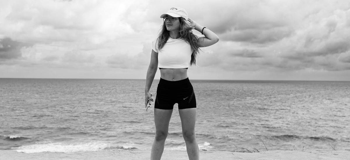 A woman in athletic attire poses near the ocean with a dramatic sky in Natal, Brazil.
