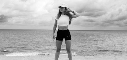 A woman in athletic attire poses near the ocean with a dramatic sky in Natal, Brazil.
