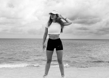 A woman in athletic attire poses near the ocean with a dramatic sky in Natal, Brazil.