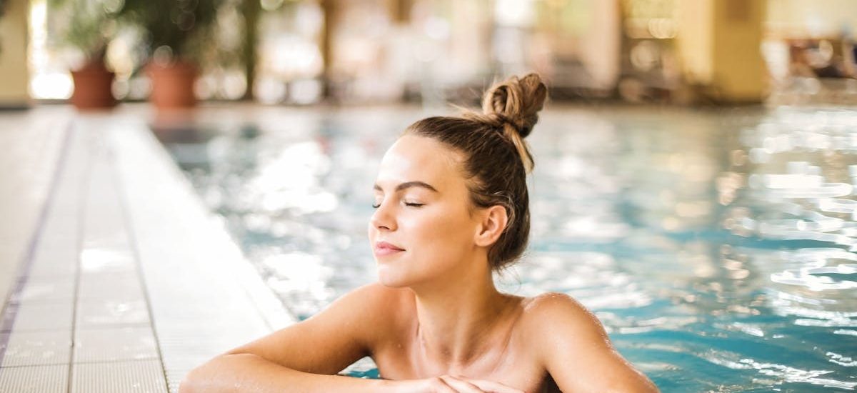 A serene woman relaxing on the edge of an indoor swimming pool, enjoying leisure time.
