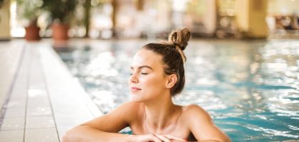 A serene woman relaxing on the edge of an indoor swimming pool, enjoying leisure time.