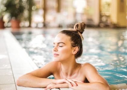 A serene woman relaxing on the edge of an indoor swimming pool, enjoying leisure time.